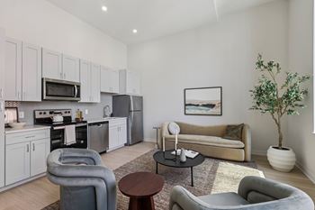 A modern living room with grey and white furniture and a kitchen area in the background. at LiveWell Apartments, Pennsylvania